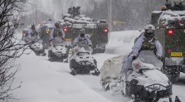 Soldater på snøscooter og cv-90 panservogner i kolonne i tett snøvær.