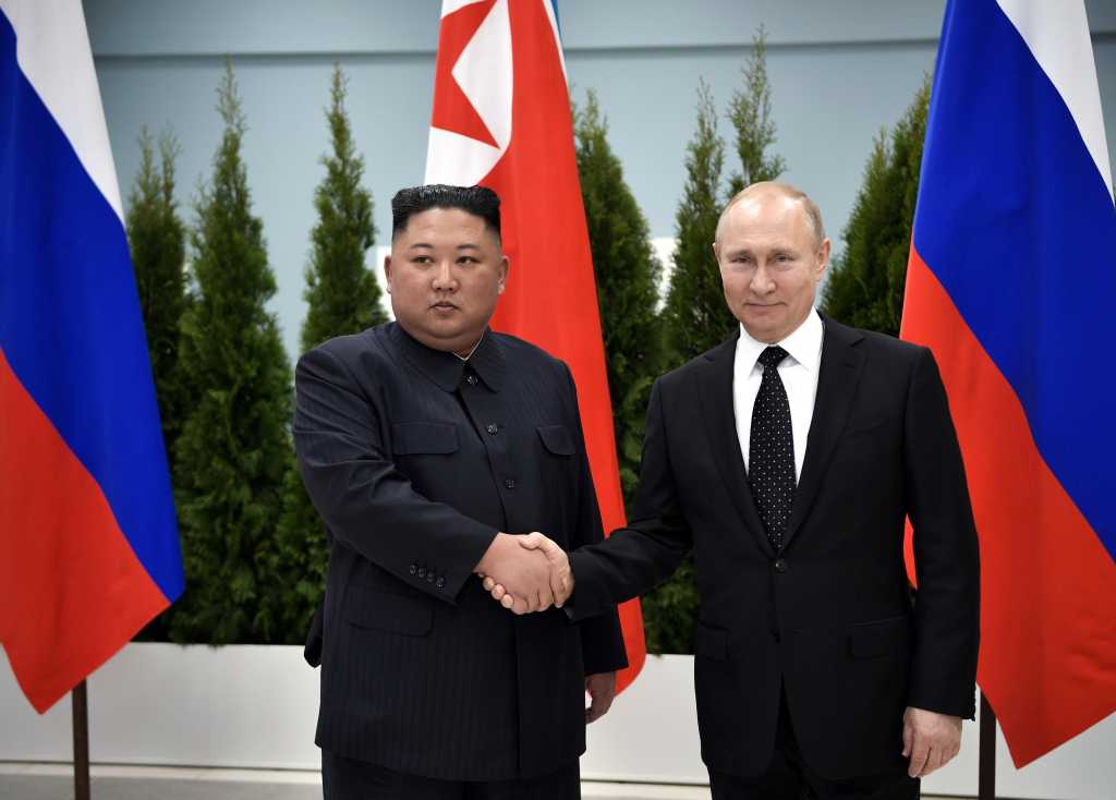 Kim-Jung Un og Vladimir Putin tar hverandre i hendene foran flaggene til de to nasjonene