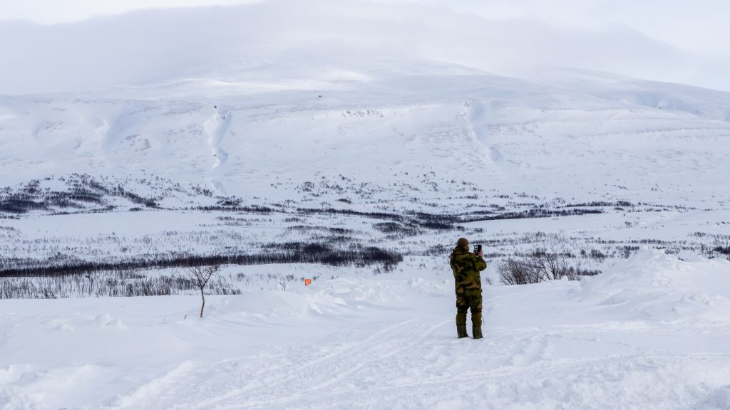 En enslig soldat tar bilde av utsikten over Halkavarre skytefelt. I bakgryunnen snødeklte fjell og vidde.