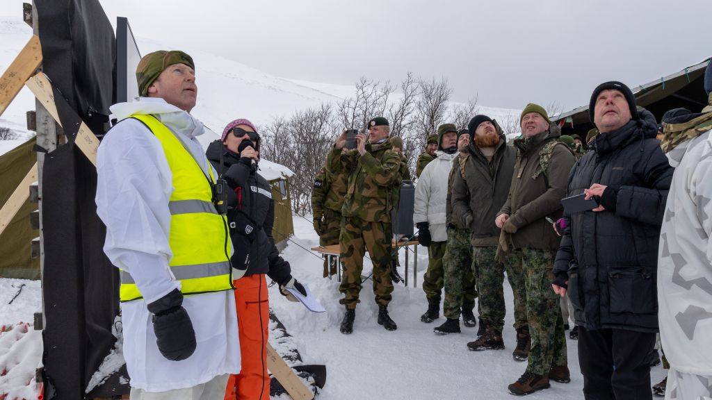En gruppe mennesker. Vinterlandskap. Alle ser opp mot himmelen, fordi det flyr droner der oppe.