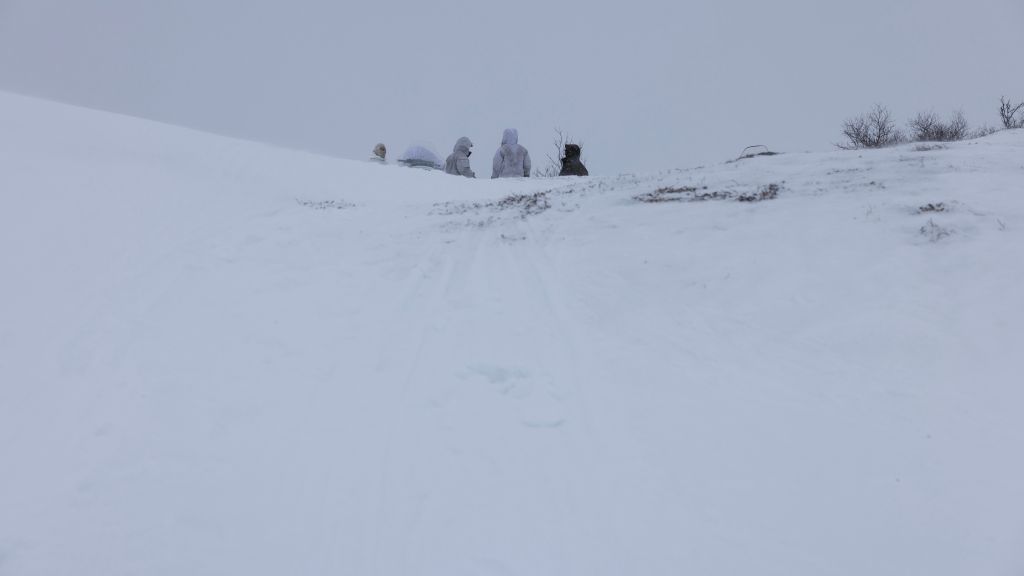 Bilde fra Halkavarre skytefelt i Finnmark. Snøføyk. Soldater er delvis skjult bak en bakketopp.
