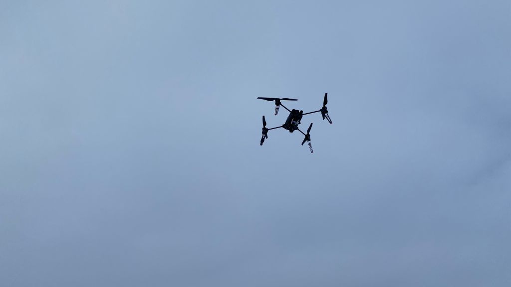Drone, kvadrokopter, svever. Grå skyer i bakgrunnen.