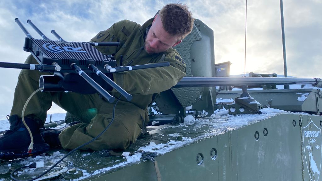 Soldat på panservogn. Skrur på antenne. Vinter. Blå himmel. Snø