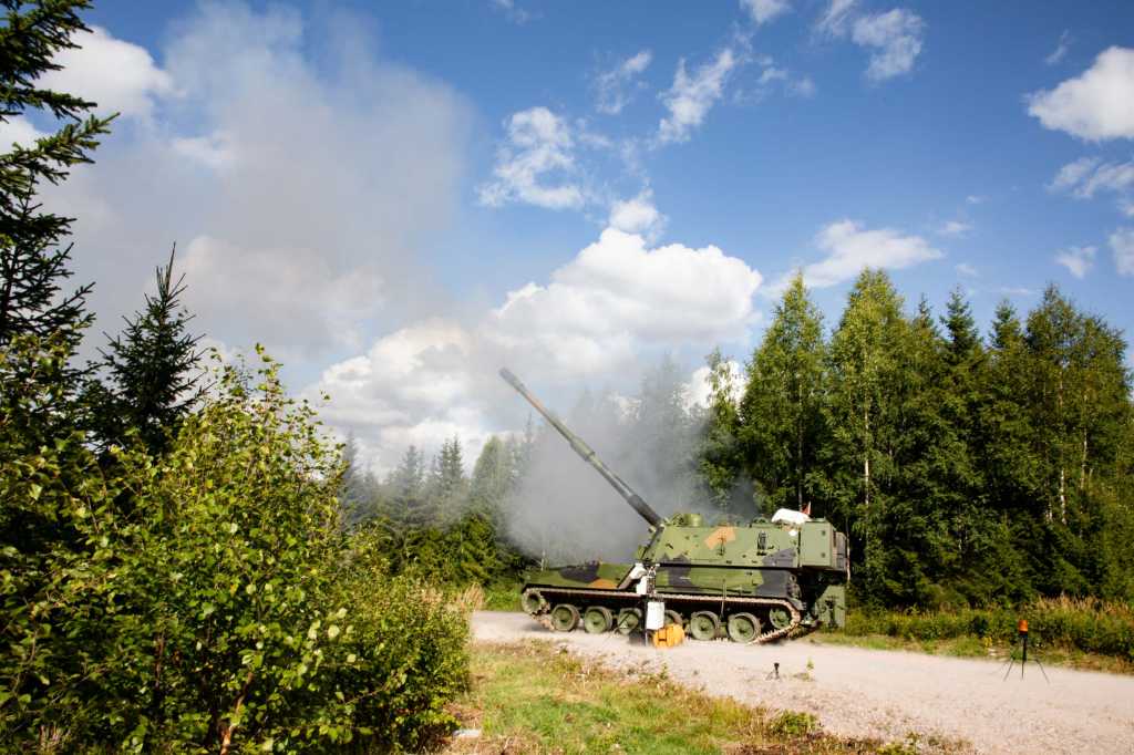 En K9 artillerivogn skyter med skarpt. Vognen har belter og den står på en grusvei i skogen.