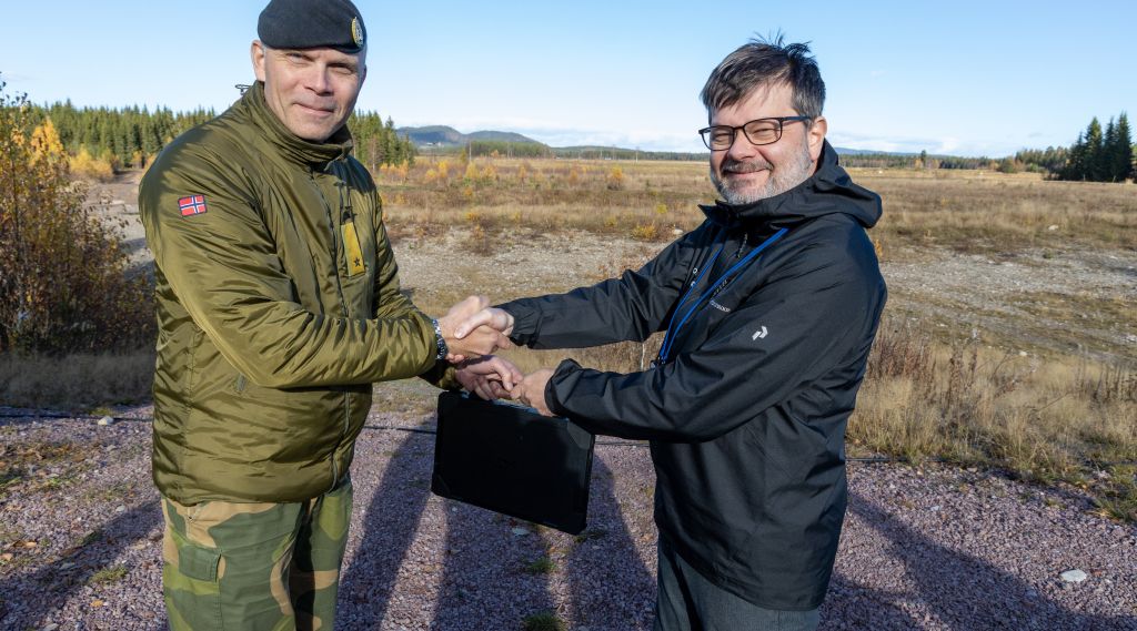 En offiser og en utvikler fra industrien håndhilser. Utendørs. Høst. Skytefelt. 