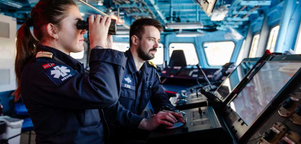 To offiserer på broen til KNM Otto Sverdrup. En kvinne med kikkert og en mann som ser på en skjerm.