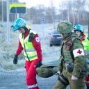 Tre personer bærer ei båre. To har sivil ambulanseuniform og en har militær uniform