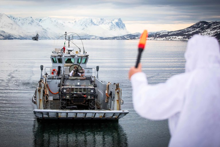 Et landgangsfartøy med et kjøretøy vinkes i land av en soldat i hvit kamuflasjeuniform.