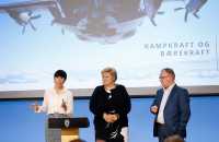 Tre politikere på scenen. Erna Solberg i blåsvart kjole i midten.
