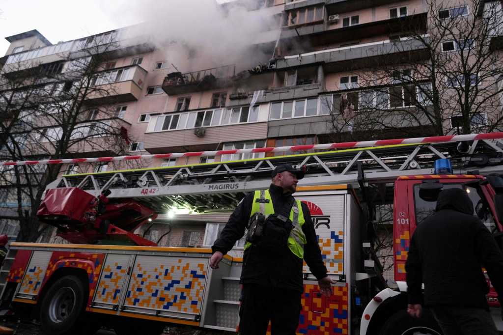 En politimann står foran en brannbil. I bakgrunnen røyk fra en boligblokk.