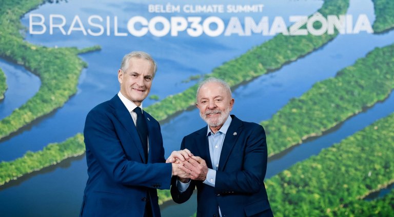 Jonas Gahr Støre og Lula da Silva holder hender foran en plakat med logoen til COP30 i Brasil.