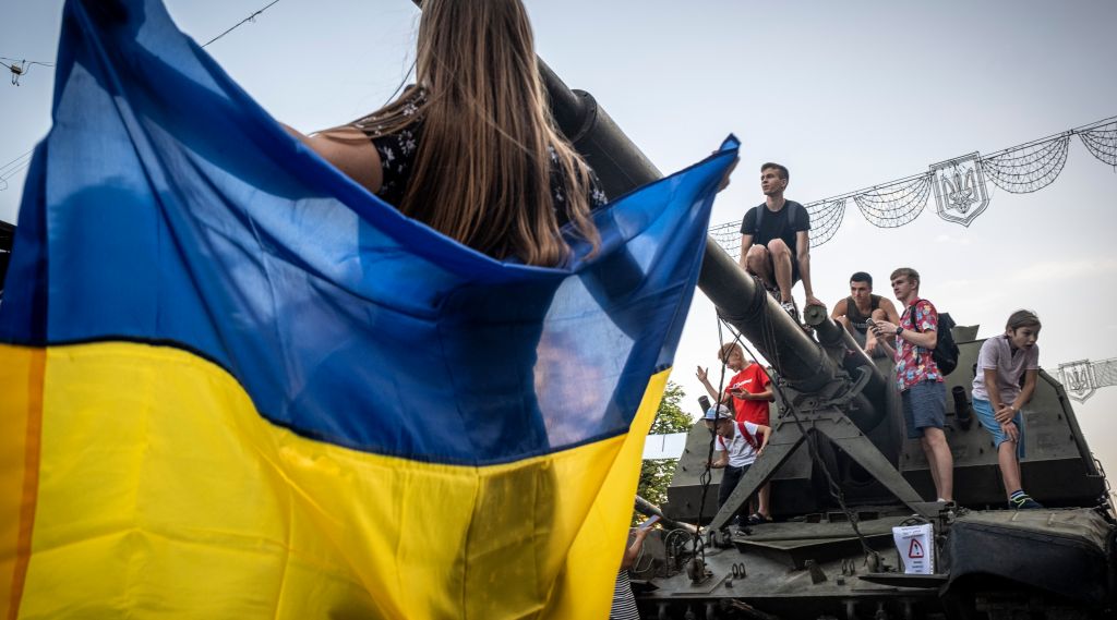 Jente holder Ukrainsk flagg. Unger og tenåringer klatrer på en beslaglagt Russisk stridsvogn som er utstilt på gaten i Kiev.