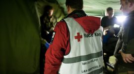 inne i et militært telt. vi ser tyggen på en med vest fra røde kors i fokus og annet militært personell rundt