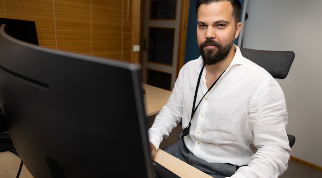 Mann i hvit skjorte sitter bak tastatur og ser rett i kamera