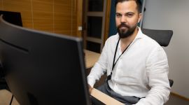 Mann i hvit skjorte sitter bak tastatur og ser rett i kamera