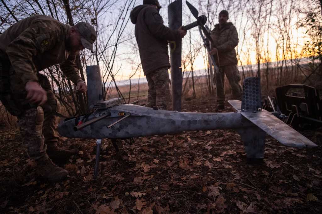 Tre soldater gjør klar en bombedrone ved fronten i ukraina. Høst. Solnedgang. Skog.