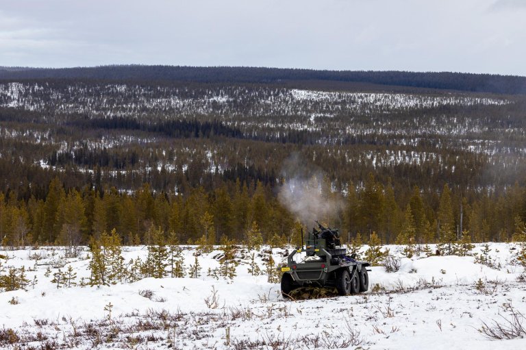 Ubemannet kjøretøy med våpenstasjon fyrer av skudd. UGV-en er står i åpent skogsterreng.
