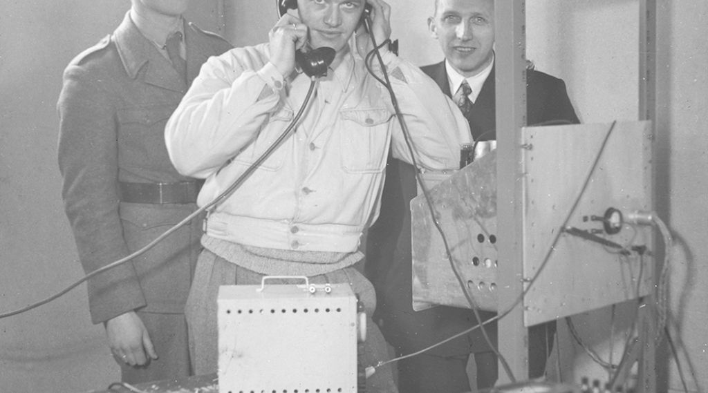 Fra utviklingen av et telesamband. Tre forskere bak en radio.