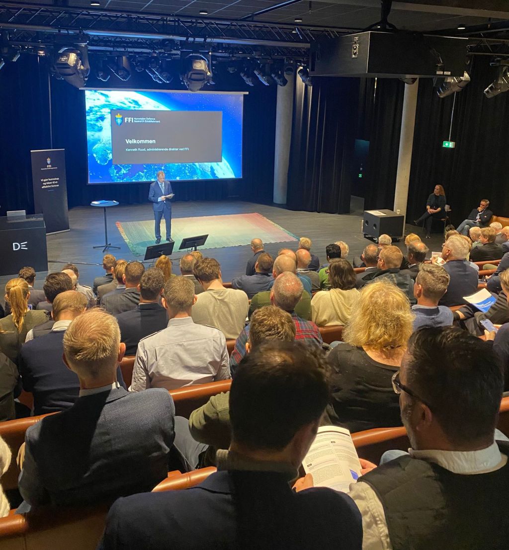 Bakhoder av folk i konferansesal og en mann i dress på scenen