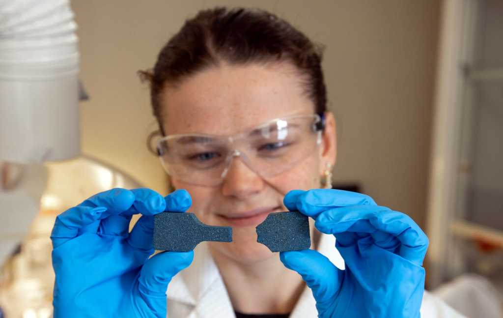 Ein forskar med vernebriller held to bitar av eit stoff mellom hendene.