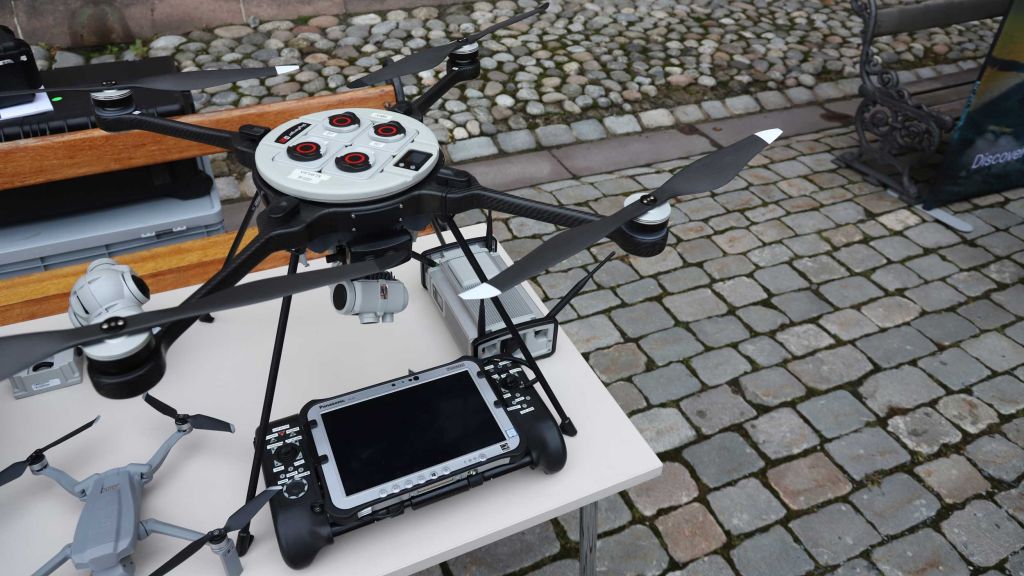 En stor drone står på et bord. En fjernkontroll med skjerm ligger foran dronen.