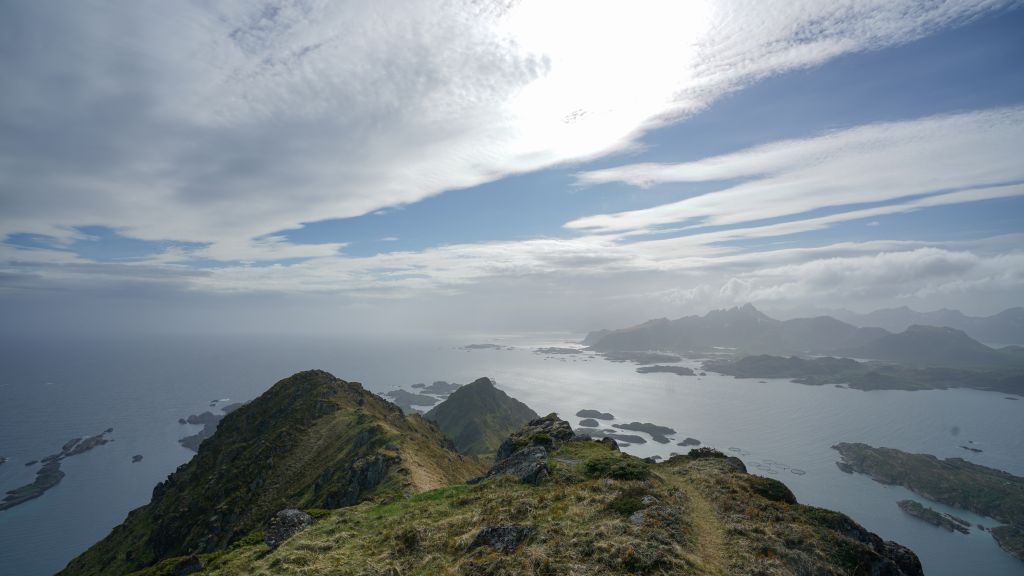 Utsikt fra fjeltopp i Lofoten. Sold, skyer, himmel og blått hav.