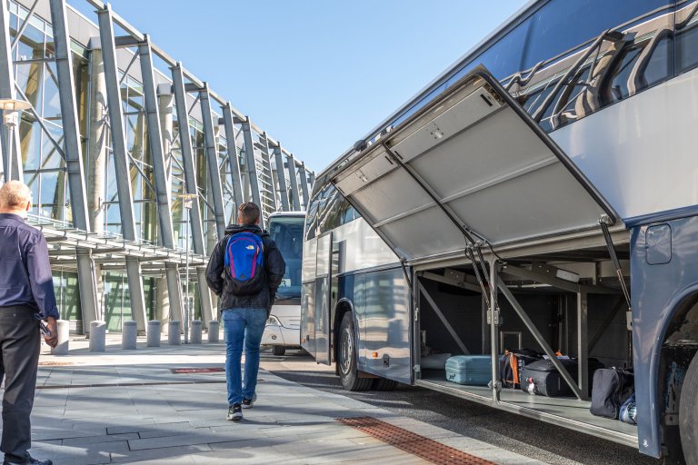 Mann med ryggsekk som går bort fra en buss med åpne bagasjeluker.