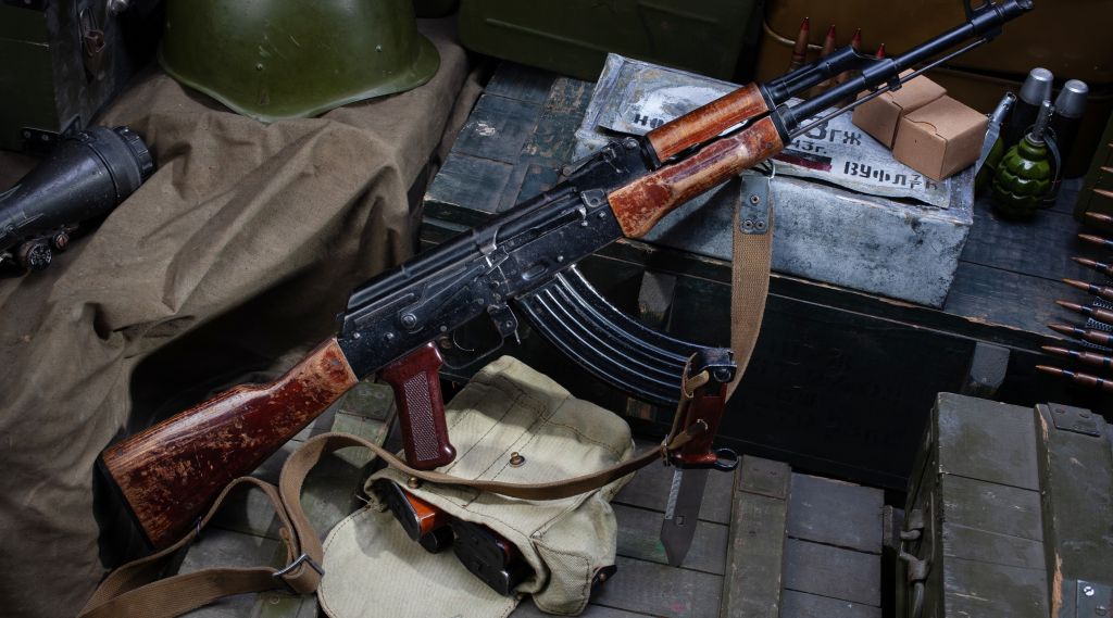 Kalashnikov AK 47 med ammunisjon på en militærgrønn boks bakgrunn. Tekst på ammunisjonsboksen på russisk - patron type og kaliber med partinummer.