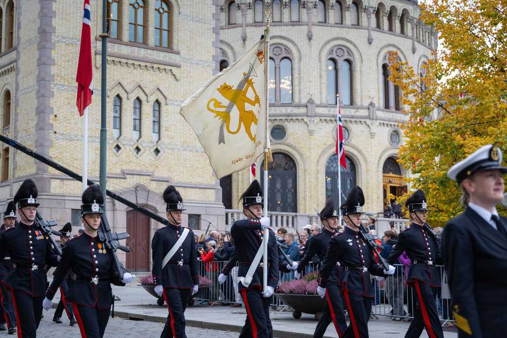 Garden marsjerer forbi Stortinget med en fane.