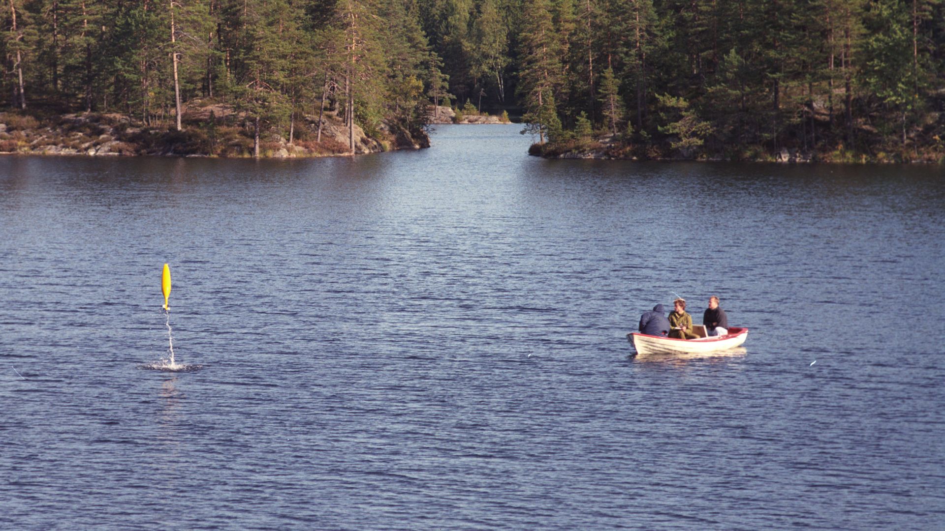 En gul ubåtmodell popper opp av vannet i Bølertjern likeved en robåt der det sitter to forskere og en soldat.