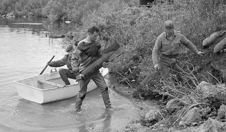 historisk bilde av folk som ryyder, eller dumer?, ammunisjon i et vann ved kirkenes. Svart hvitt. 