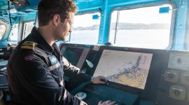 inne på broen i en fregatt. En mann står og ser på et sjøkart