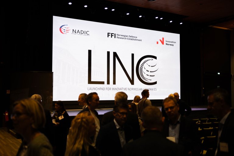 Mingling foran en presentasjon som viser LINC-logoen og logoen til NADIC, FFI og Innovasjon Norge.