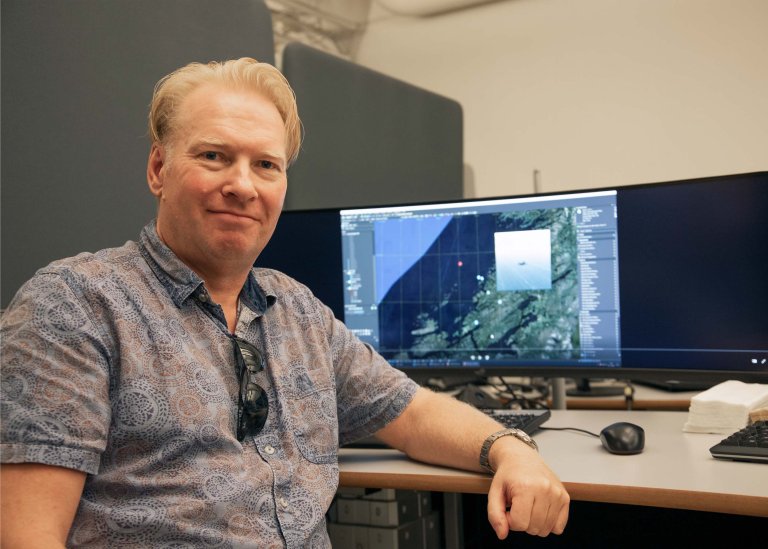 Forsker med PC-skjerm i bakgrunnen som viser et kartutsnitt.