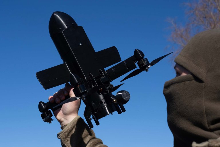 En maksert person holder opp en svart avskjæringdrone. 