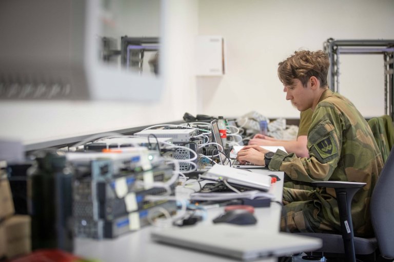 Soldat som sitter ved en pult der det ligger en del IT-utstyr.