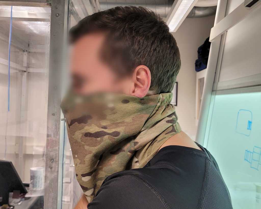 En testperson står med en SAFEgaiter kamuflasbuff med åndedrettsvern i ett av FFIs laboratorier. Ansiktet er sladdet.