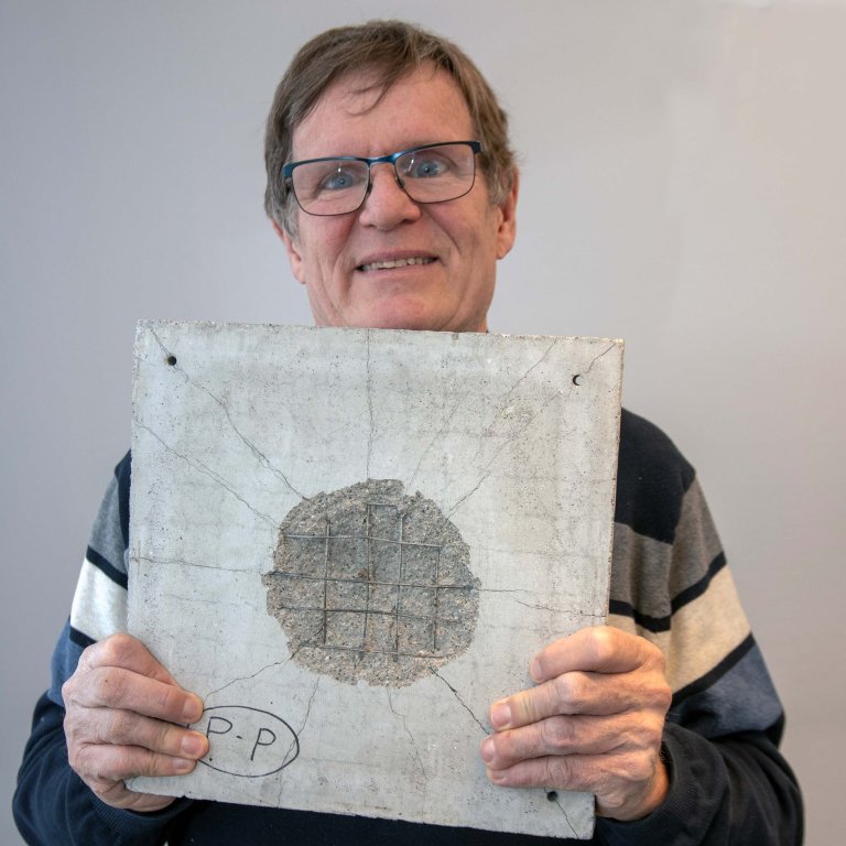 Henrik holder opp en betongplate med synlige skader og der armeringen viser.