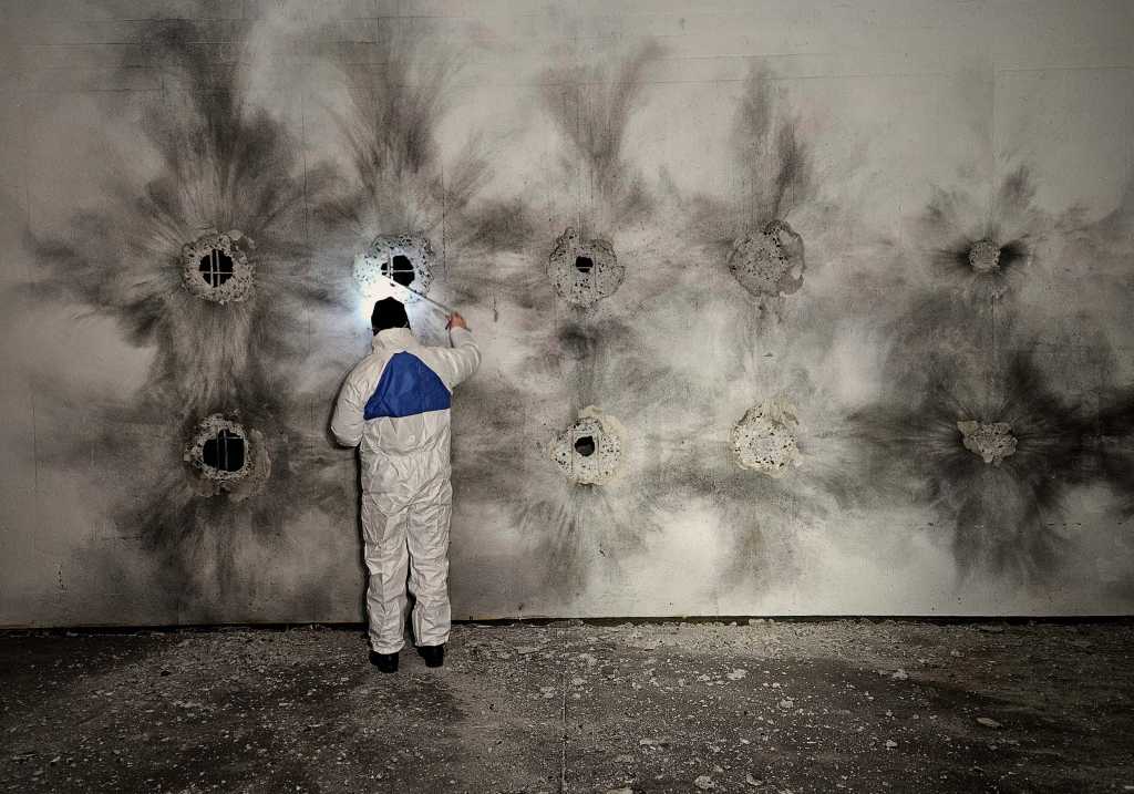 En mann i kjeledress undersøker en betongvegg etter et spreningsforsøk.