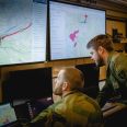 To menn i militæruniform sitter og ser på skjermer med militære kart og informasjon