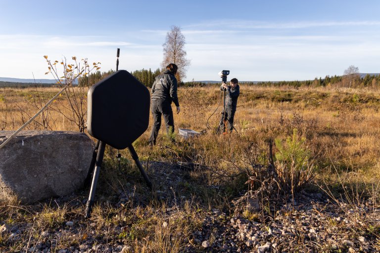 To forskere står i høstlandskap og ordner med noen stativ