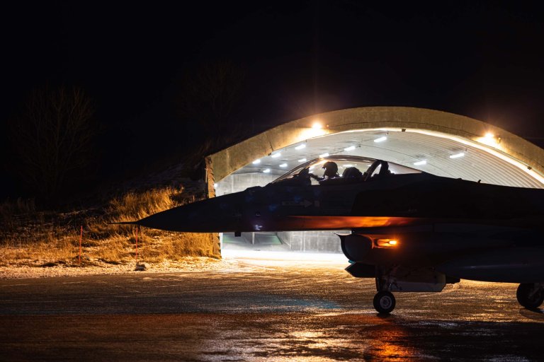 Eit kampfly framfor ein hangar om natta.