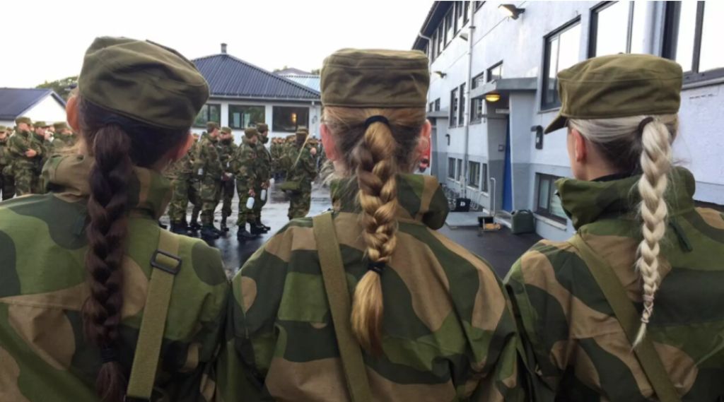 Vi ser ryggene til tre kvinner i hærens militære kamuflasjeuniform. de står skulder til skulder og alle tre har lange fletter som henger ned.