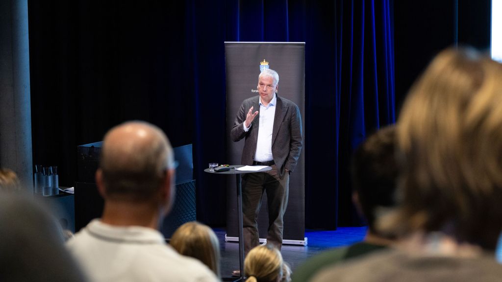 Helge Danielsen på scenen under Påvirkningskonferansen 2026. Han står ved et bord. Publikum i forgrunnen.