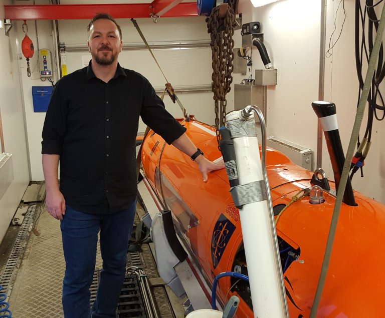 Forsker ombord på skip, ved siden av en orange minubåt.