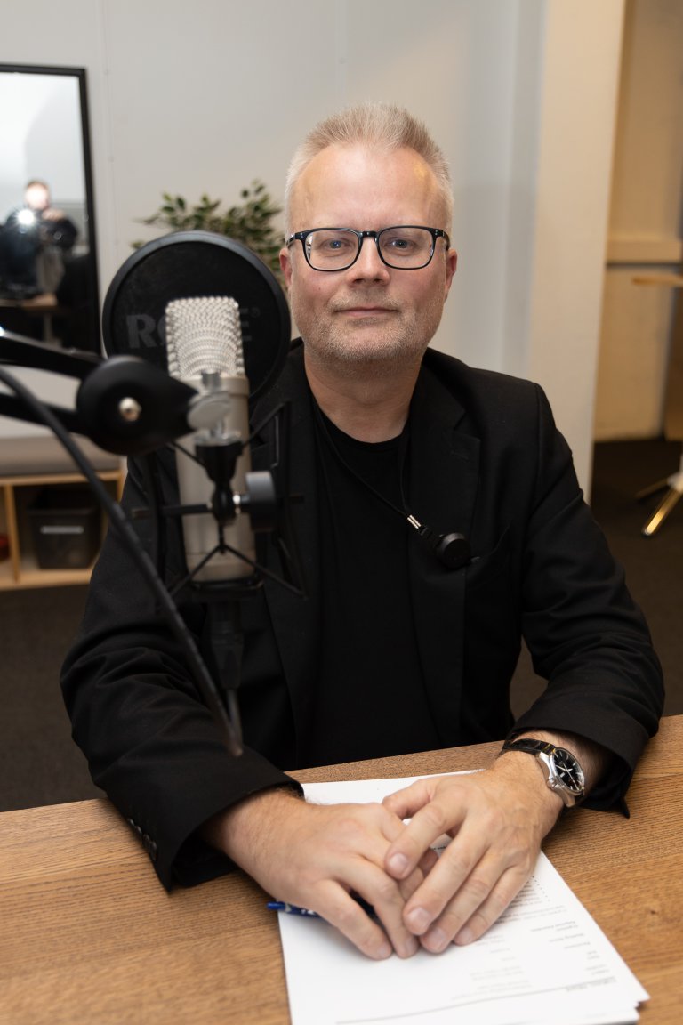Portrett av Håvard Fridheim i podkaststudio. I forgrunnen ser vi en mikrofon.