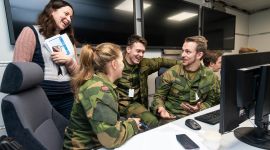 En forsker og tre studenter i uniform, foran pc