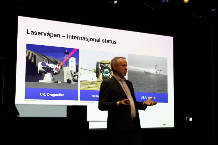 Espen Lippert på scenen i Deichmansalen. I bakgrunnens er vi et lysbilde med eksempler på laservåpen.