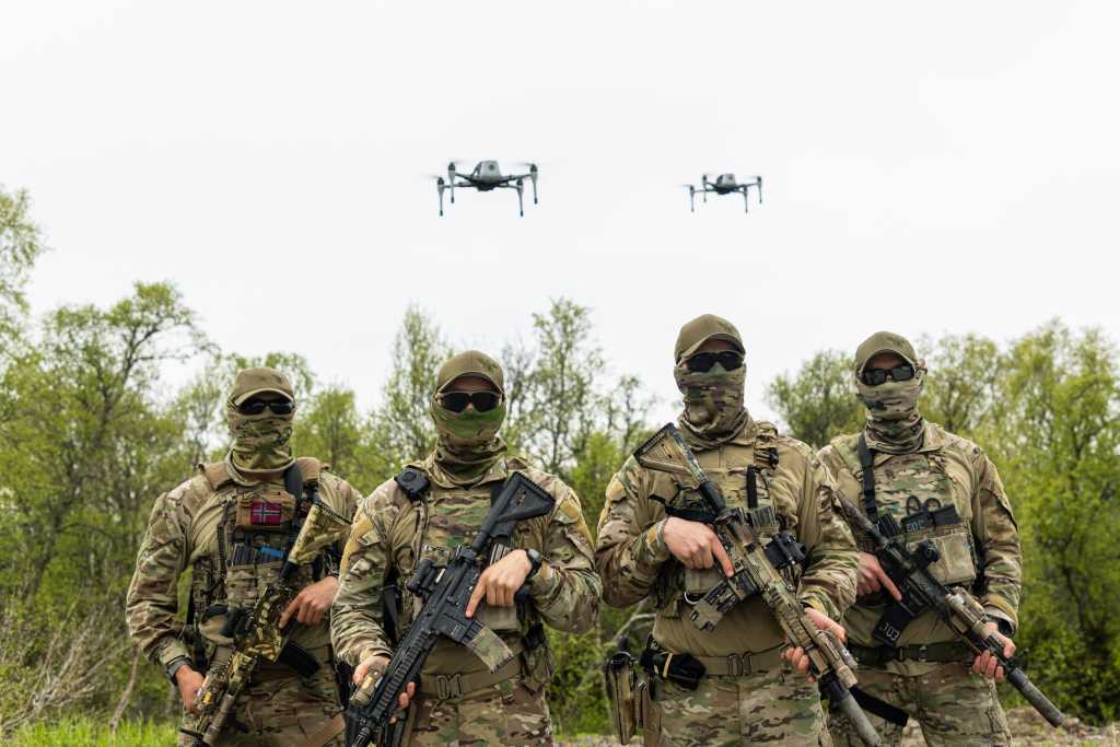 Fire maskerte kystjegere med våpen. I luften over dem svever to droner.