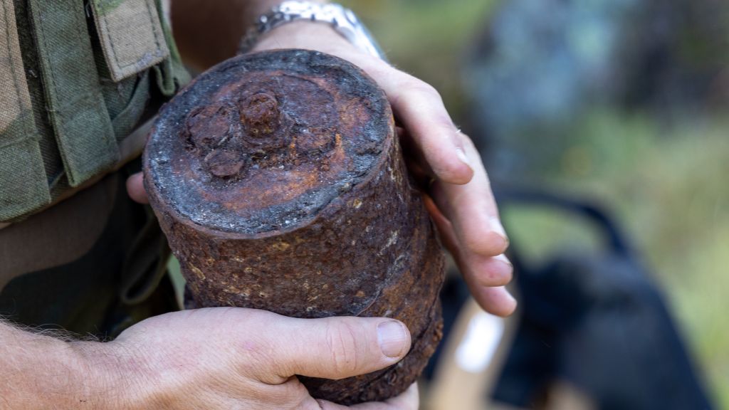 Nærbilde av en rusten mine, holdt av en soldat.